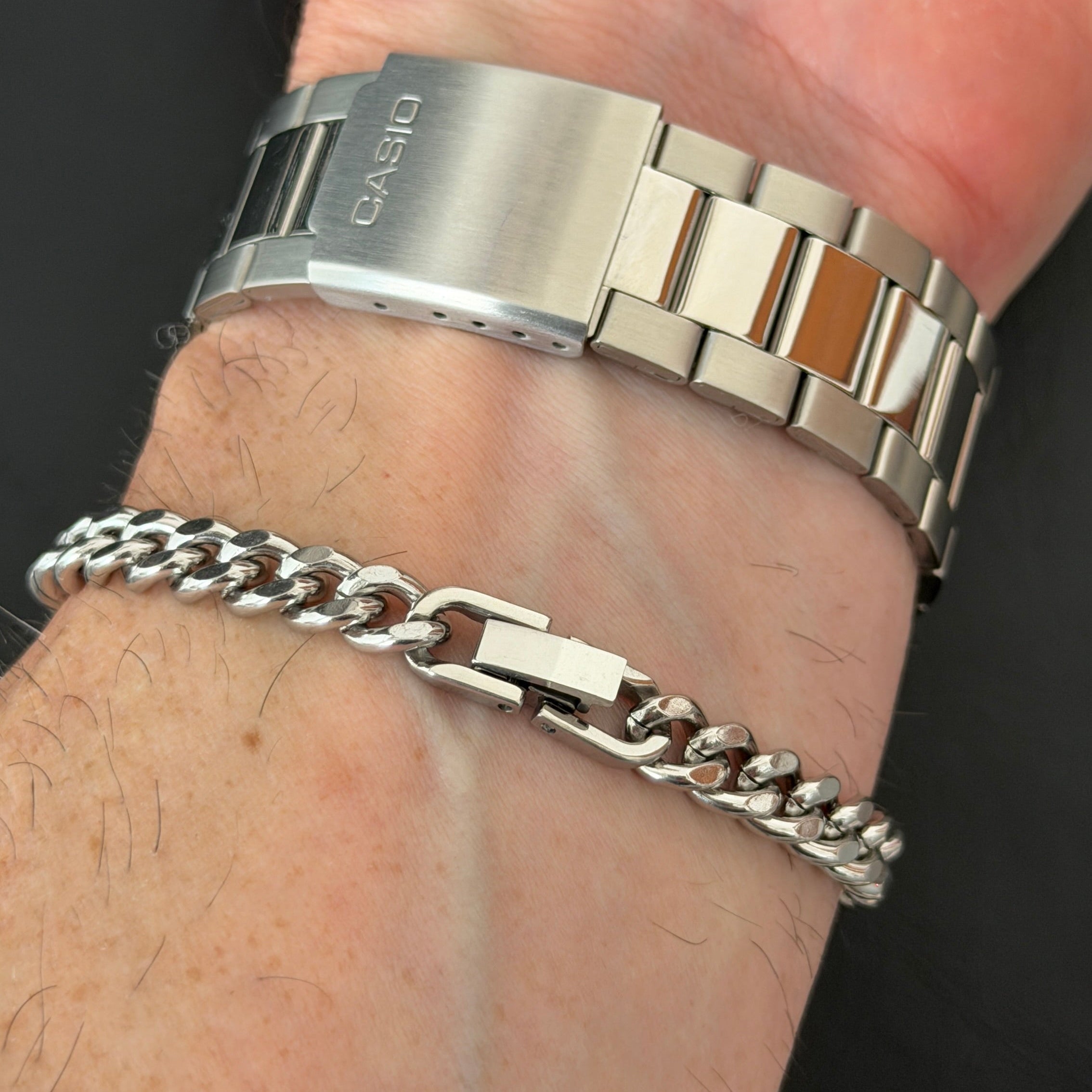 Close-up of a wrist wearing two silver bracelets on a dark background