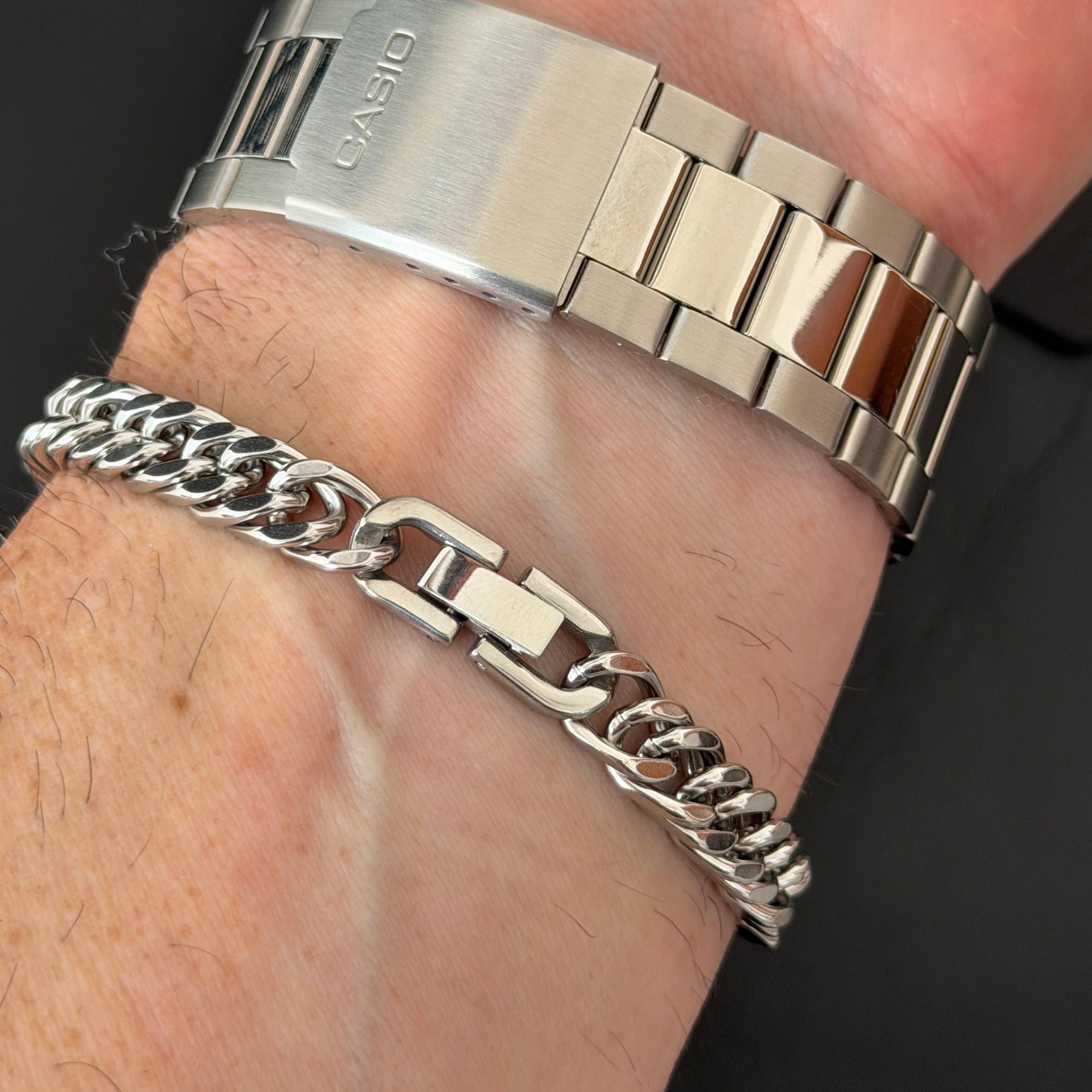 Silver watch and bracelet on a wrist against a dark background