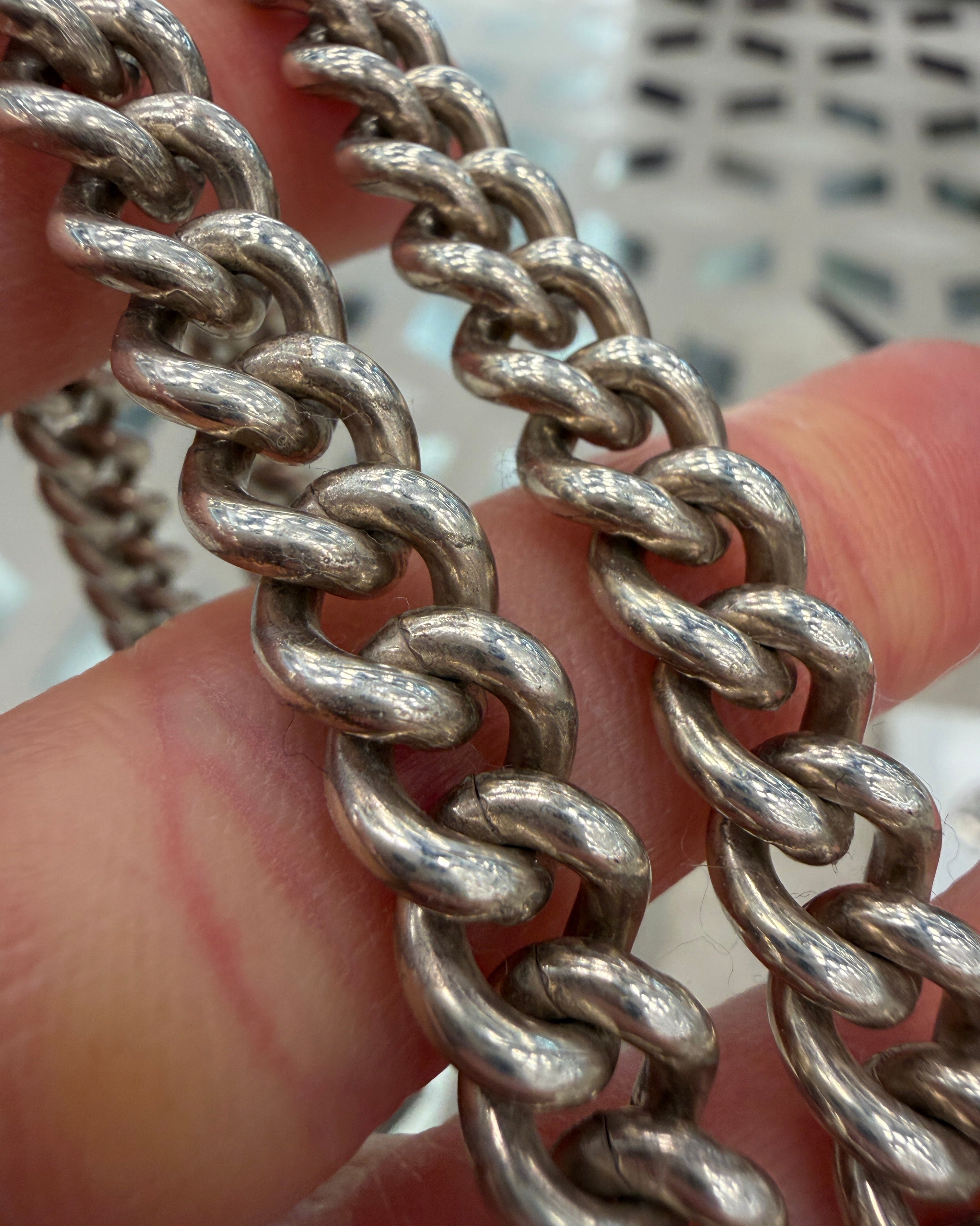 Close-up of a silver chain held between fingers with a blurred background